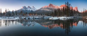 snowy scene with mountains in the background and trees and a river in the foreground
